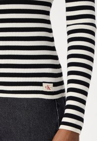 Top a maniche lunghe a righe bianche e nere, con una piccola etichetta CK Jeans all'orlo. La texture è liscia e aderente.