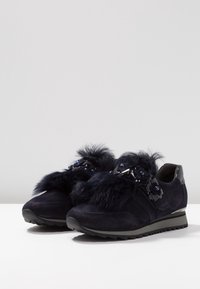 Navy suede sneakers feature a plush fur accent, decorative flowers with shiny details, and a textured sole for grip and support.