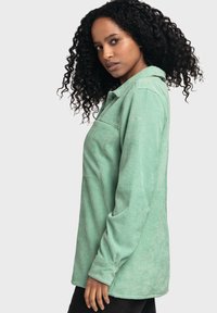 Light green corduroy shirt with long sleeves, collar, and a pocket detail. Soft texture and vertical ribbed pattern.