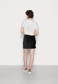 T-shirt curta branco com estampa tie-dye, combinada com uma mini saia preta em camurça e ténis brancos com detalhes castanhos. Vista pela parte de trás.