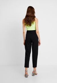Svarta högmidjade byxor med en elegant design, tillsammans med en neongrön åtsittande topp och randiga klacksandaler. Slät tyg och skräddarsydd passform.