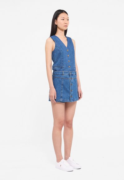 denim dress with buttons, V-neck, sleeveless design, light blue color, features two side pockets, paired with white shoes.