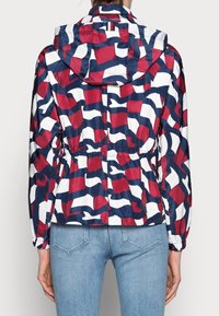 Bunda s kapucí v červené, bílé a námořnické modré barvě s vzorem, elastickým pasem a dlouhými rukávy. Hladký, lesklý materiál. Vzory bílé vlny.