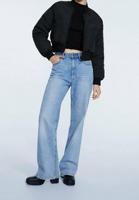 Zwarte cropped pufferjas met geribbelde manchetten, gecombineerd met lichtblauwe, hooggetailleerde flare jeans en grove zwarte plateauzolen.