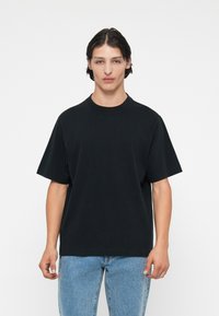 Mustan puuvillane T-särk, millel on ümmargune kaelus ja lühikesed varrukad, koos helesiniste denim-jiinidega. Lihtne kujundus, nähtavad mustrid või aksessuaarid puuduvad.