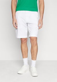 Hvide knælange shorts med flad front, bæltestropper og sidelommer. Bæres med en grøn t-shirt og hvide sneakers, som har struktureret stof.
