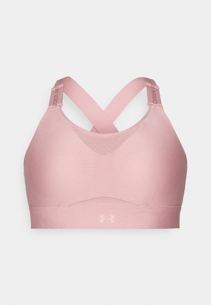 Vaaleanpunainen urheilbra, jossa on sileä ja joustava kangas; erityispiirteenä ristikkäiset hihnat ja logo vyötäröllä. Suunnittelussa on etusijalla mukavuus ja tuki.