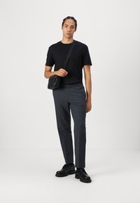 Camiseta negra, pantalones grises con estampado y zapatos negros. Se lleva una pequeña bandolera negra de manera diagonal sobre el cuerpo. Estilo sencillo y moderno.