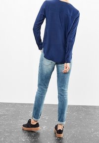 Mörkblå skjorta med långa ärmar i mjukt tyg, kombinerad med ljusblå jeans. Svarta skor med brun sula. Enkelt design, inga mönster.