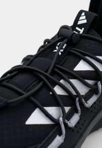 Black athletic shoe with textured material, elastic laces, and reflective white accents in a triangular pattern on the upper.