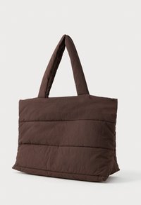 Velká hnědá quiltovaná taška přes rameno s polstrovanými uchy, jednoduchý design, vystavená na čistém bílém pozadí.