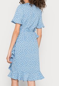 Robes bleu clair avec un imprimé floral, manches courtes à volants, taille nouée et ourlet à volants évasé. Fabriquée en tissu doux.