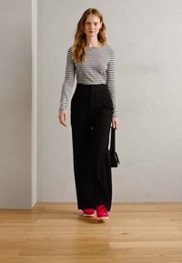 Pantaloni neri a gamba larga, top a maniche lunghe a righe bianche e nere, e scarpe da ginnastica rosa brillante. La modella porta una piccola borsa nera.