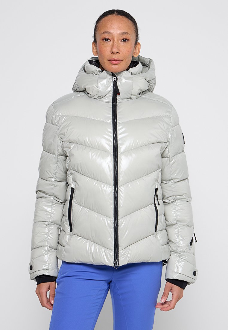 Jacke mit Polsterung in Hellgrau mit glänzender Oberfläche. Verfügt über einen hohen Kragen, einen Reißverschluss vorne und schwarze Akzente an den Reißverschlüssen und Ärmelbündchen.