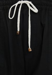 Pantalones negros con cinturilla elástica y cordón blanco. Los extremos del cordón tienen cuentas decorativas marrones. Incluye bolsillos en los lados.