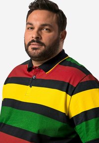 Bavlněná polo košile s horizontálními pruhy v červené, žluté, zelené a černé barvě. Mezi výrazné detaily patří černý límec a dva knoflíky.