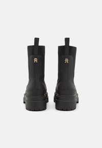 Bottines noires à cheville en cuir mat, avec des panneaux latéraux élastiques et une semelle en caoutchouc épaisse. Présentent un accent de logo doré à l'arrière.