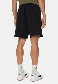 Shorts deportivos negros, con cintura elástica, de longitud a la rodilla, combinados con zapatillas blancas y calcetines. Diseño simple, textura similar al algodón.