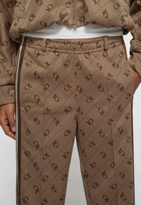 Brązowe spodnie w wzory wykonane z teksturowanej tkaniny, z motywem diamentów i logo "10", bocznymi paskami oraz elastycznym paskiem w talii.