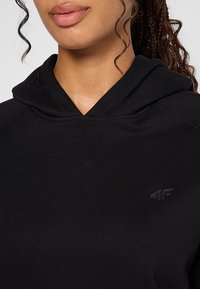 Czarna bluza z kapturem o miękkiej fakturze, z przednią kieszenią i małym, wytłoczonym logo na lewej piersi.