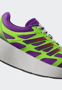 Lila och grön sportskor med överdel i mesh, kontrasterande plastdetaljer, tjock vit sula och flerfärgad design på sidorna.