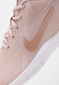 Baskets en maille rose clair avec des accents ton sur ton, dotées d'un grand logo swoosh beige, d'un bout arrondi et d'une semelle extérieure blanche texturée.