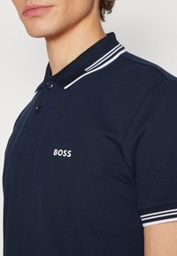 Námornícky polo tričko s bielymi gombíkmi, pruhovaným golierom a bielym logom "BOSS". Hladká, štruktúrovaná tkanina, s klasickým strihom.