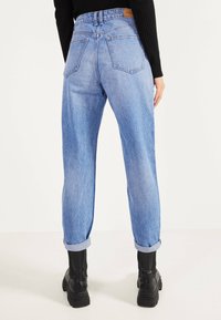 Ljust blå denimjeans med avslappnad passform, hög midja, uppvikta benslut och två bakfickor, kombinerat med svarta kraftiga stövlar.
