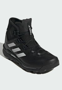 Czarne buty trekkingowe z wysokim cholewką, siateczkową cholewką, odblaskowymi srebrnymi akcentami i wytrzymałą podeszwą zapewniającą przyczepność na różnych nawierzchniach.
