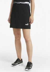 Skort negro con camiseta que presenta una cinturilla elástica y un logo de Puma en blanco. Combinado con zapatillas deportivas negras y un diseño minimalista.