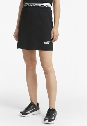 Skort negro con camiseta que presenta una cinturilla elástica y un logo de Puma en blanco. Combinado con zapatillas deportivas negras y un diseño minimalista.