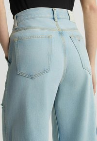 Jeans de cintura alta en azul claro con un corte relajado. Presentan grandes bolsillos traseros, costuras sutiles y una cinturilla suave con cierre de botón.