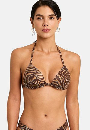 Femme portant un haut de bikini à imprimé animal marron et beige à dos nu avec des boucles d'oreilles créoles dorées sur un fond clair uni.