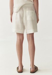 Linen shorts in light beige, featuring an elastic waistband and a single back pocket. Cuffs are finished with a contrasting band.
