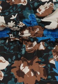 Tissu de robe fleurie avec de grandes fleurs marron, blanches et bleu sarcelle sur un fond noir, avec une ceinture élastique et des bords volantés bleus.