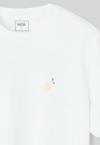 T-shirt blanc à manches courtes en coton, présentant un petit graphique de citron jaune avec des feuilles vertes sur la poitrine gauche.