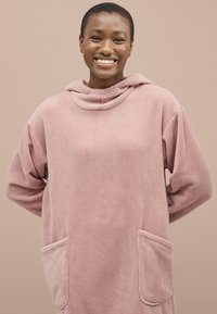 Overdimensioneret lyserød fleece hoodie med en rund hætte, sidelommer og blødt materiale, der har lange, løse ærmer og en afslappet pasform.