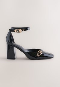 Black patent leather high-heeled shoe with ankle strap, square toe, gold buckle accents, and a chunky heel. Smooth, glossy texture.