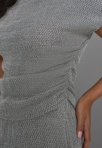 Robe tricotée grise texturée avec un motif en nid d'abeille, ornée de détails froncés à la taille et de manches courtes. Tissu lisse et ajusté.