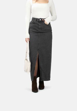 Jupe maxi en denim gris avec une fente frontale, taille haute et design à cinq poches. Associée à un haut à manches longues blanc et des bottes à chevilles marron.