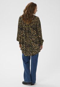 Langärmeliges Hemd mit einem schwarz-goldenen Zebramuster, locker sitzend, mit geschichtetem Rücken, kombiniert mit weit geschnittenen blauen Jeans und schwarzen Schuhen.