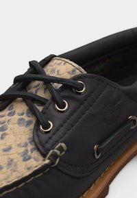 Σκούρο δερμάτινο παπούτσι τύπου boat με γλώσσα από ύφασμα με λεοπάρ σχέδιο, μαύρα κορδόνια διαπερασμένα μέσα από μεταλλικά παπούτσια και καφέ λαστιχένια σόλα ορατή.