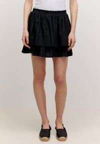 Zwarte tiered rok met een elastische tailleband, gemaakt van een textuurstof. Het ontwerp omvat twee lagen ruffles die diepte en volume toevoegen.