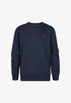 Marineblauer Pullover mit Rundhalsausschnitt und kleinem Logodetail, kombiniert mit hellblauen Denim-Jeans und weißen Sneakern.