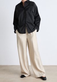 Black striped button-up shirt with shoulder accents paired with cream wide-leg trousers. Black flat shoes complete the outfit. Simple and modern design.