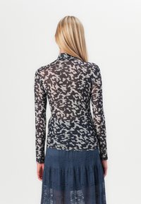 Long-sleeve, fitted top in a sheer, black and grey abstract pattern, paired with a layered navy blue lace skirt.