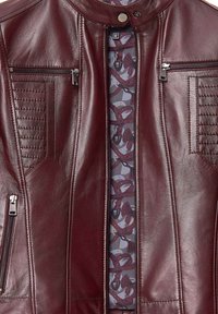 Giubbotto in pelle bordeaux con una texture liscia, dotato di tasche sul petto con zip, dettagli arricciati sulle spalle e una fodera interna a motivo.