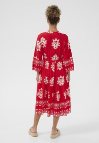 Röd knälång klänning med vita blommiga och geometriska mönster, långa trumpetärmar, insydd midja och flerlagad kjol.