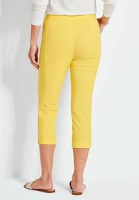 Gele cropped broek met zijnaad, slim fit en opgerolde mouwen, gemaakt van lichte stof, gecombineerd met platte sandalen.