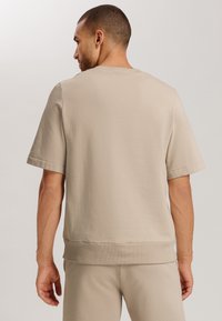Béžové tričko s krátkým rukávem vyrobené z bavlněné směsi, kulatý výstřih a žebrovaný lem, s hladkou texturou a minimalistickým designem.